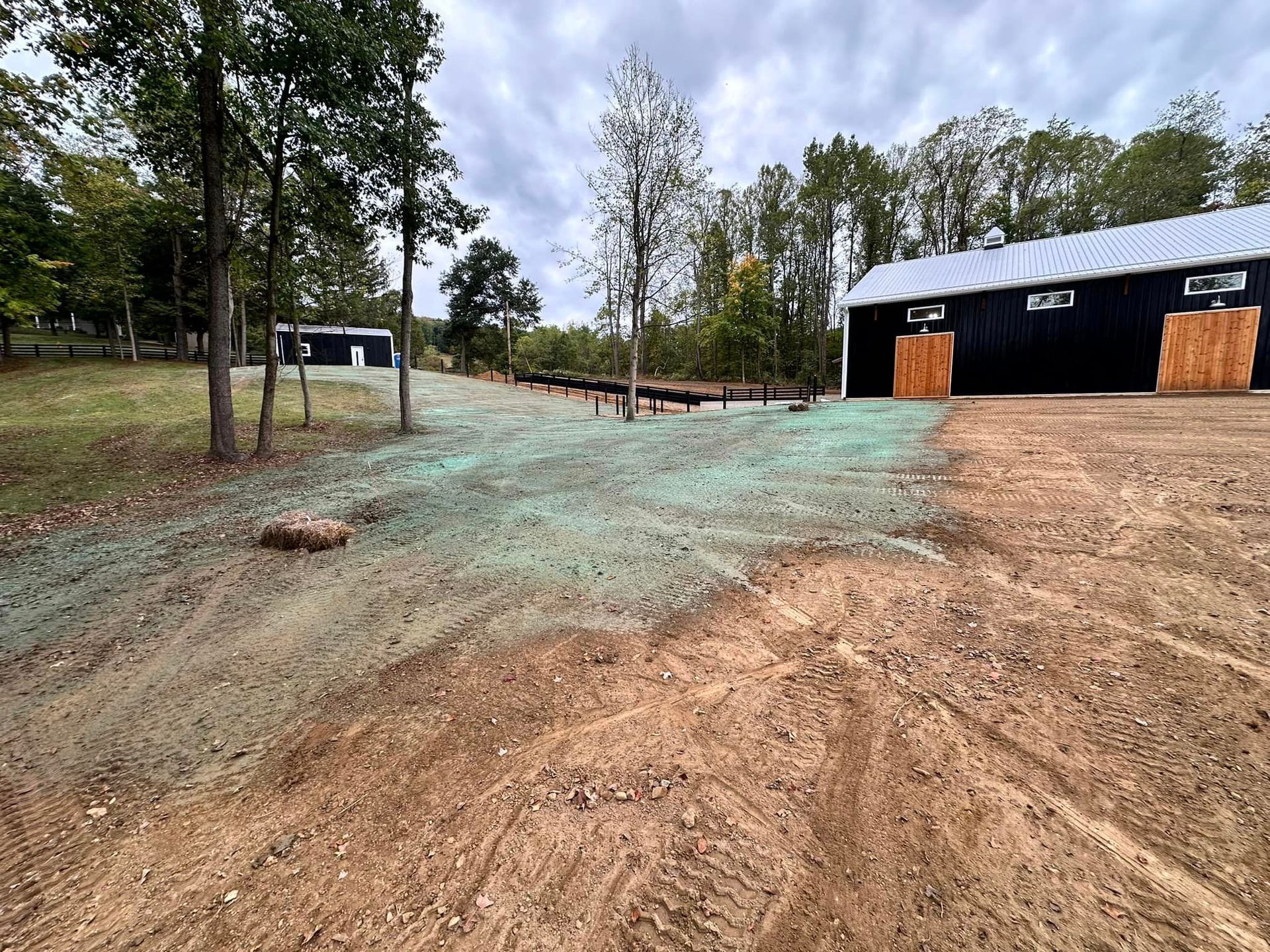 A dirt road leading to a barn with trees in the background.