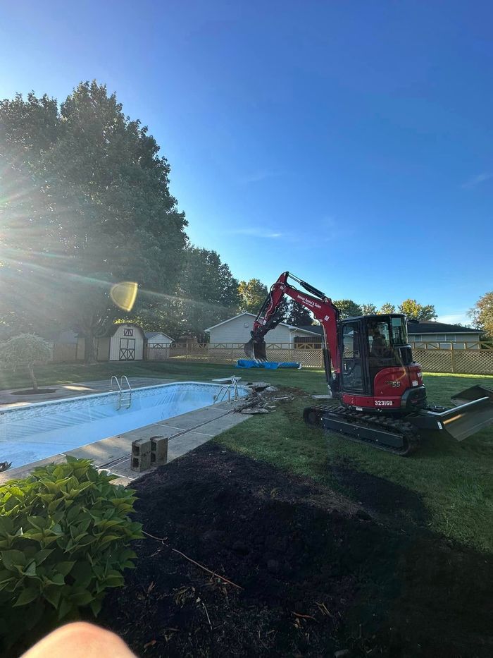 A red excavator is working in a backyard next to a swimming pool.