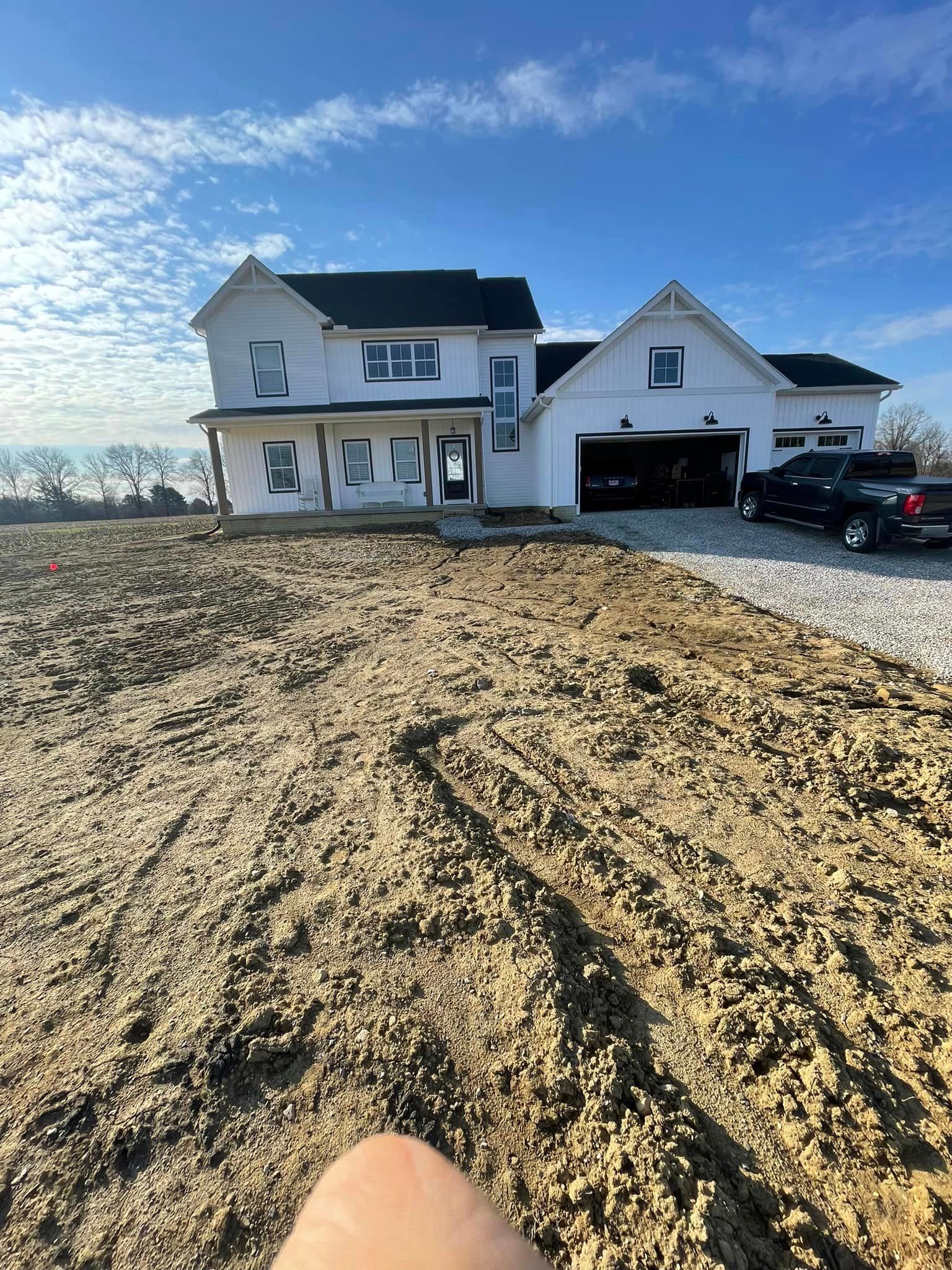 A large white house is sitting on top of a dirt field.