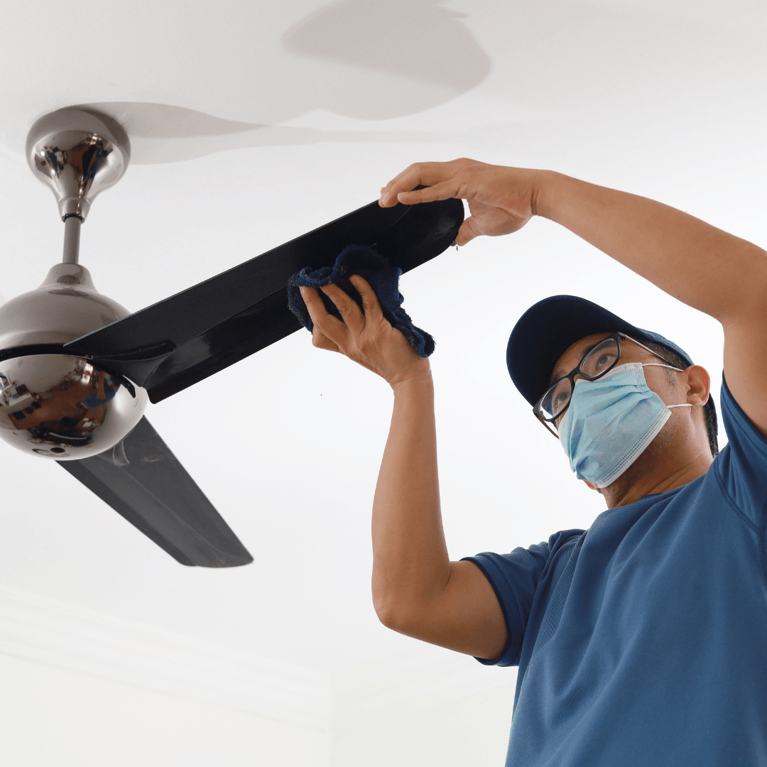 masked man cleaning ceiling fan