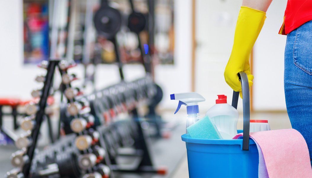 A janitorial cleaner with a yellow rubber glove holds a bucket of cleaning supplies