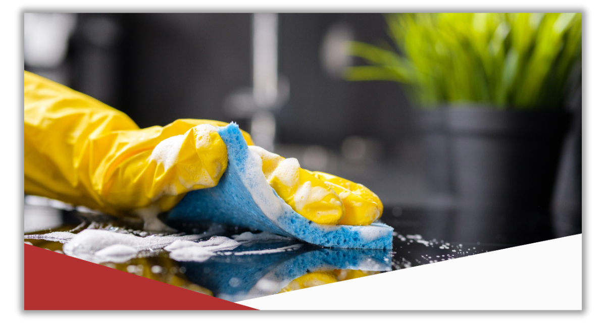 A person wearing yellow gloves is cleaning a counter with a sponge.