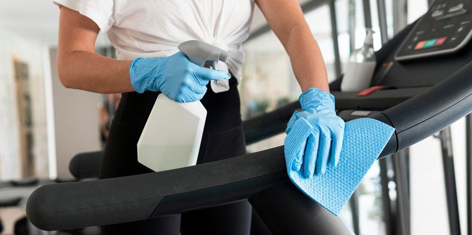 Professional cleaner wearing gloves wiping gym equipment