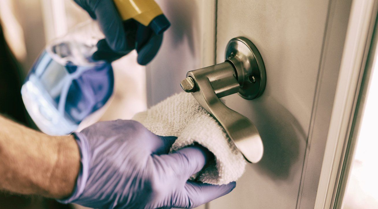 Professional cleaner with gloves thoroughly disinfecting office door knob