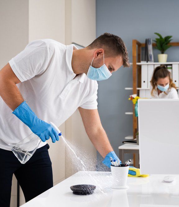 Professional office cleaners spraying and wiping desks