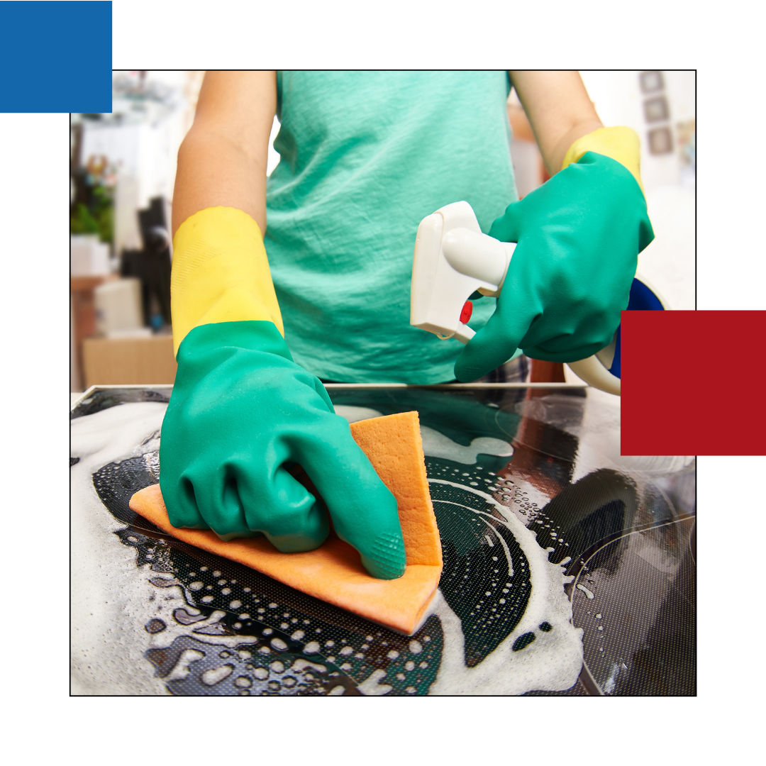 A person wearing gloves is cleaning a stove top with a sponge