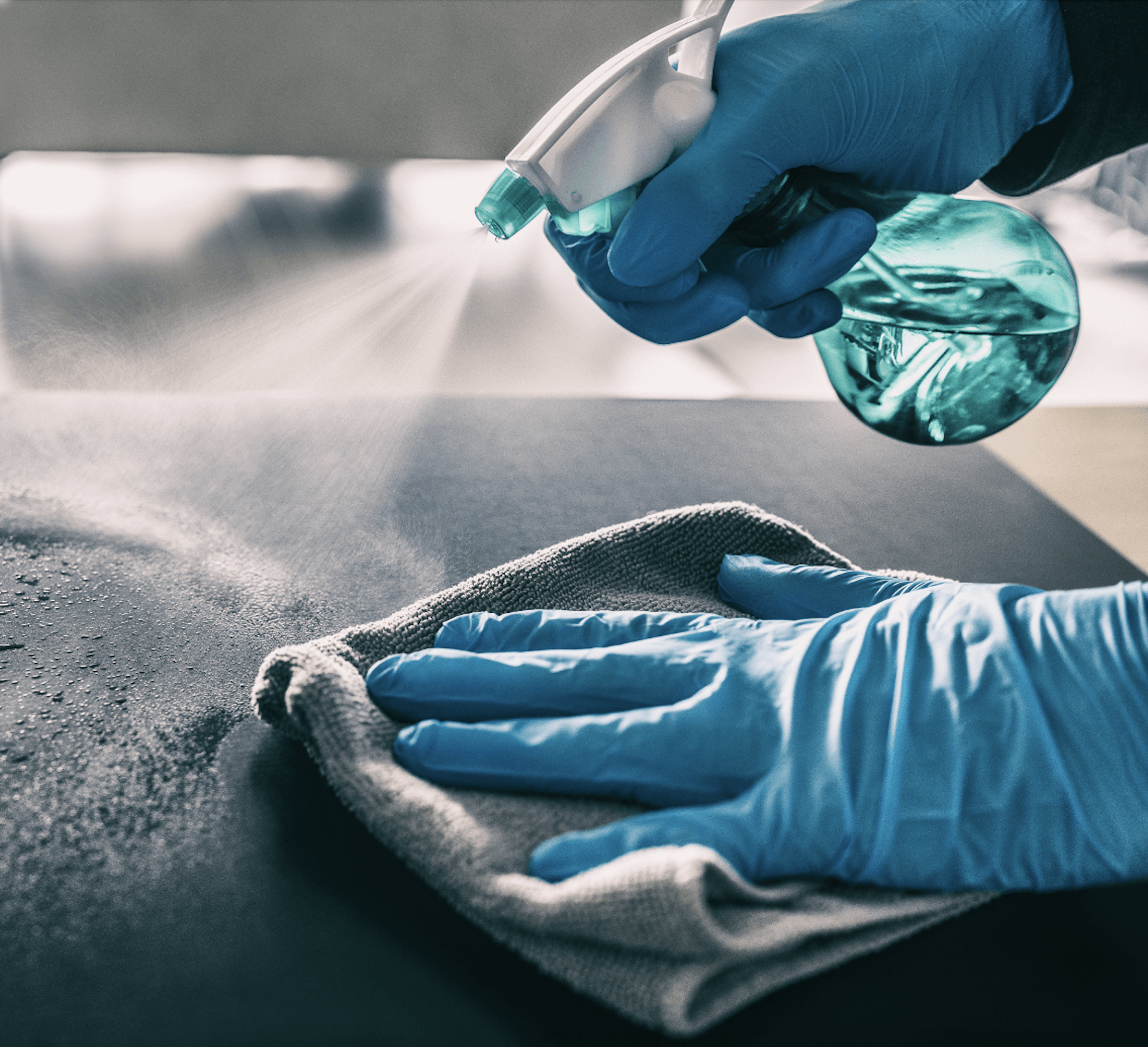 gloved hands sanitizing an office table with disinfectant spray and clean rag