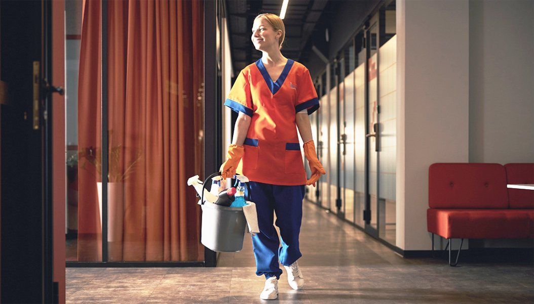 day porter holding cleaning supplies while walking across an office hallway
