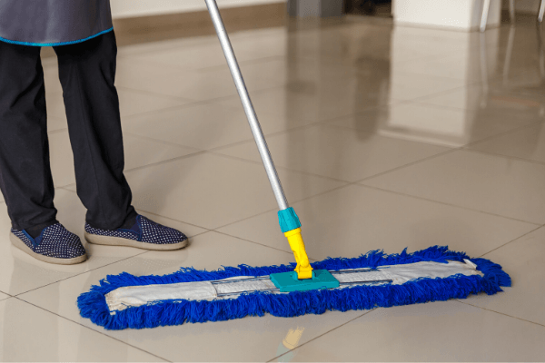The lower half of a janitor dust mopping a floor for janitorial services