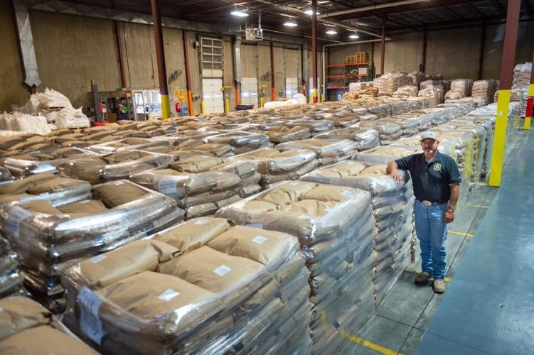 A man standing next to neatly stacked pallets of food in the warehouse.