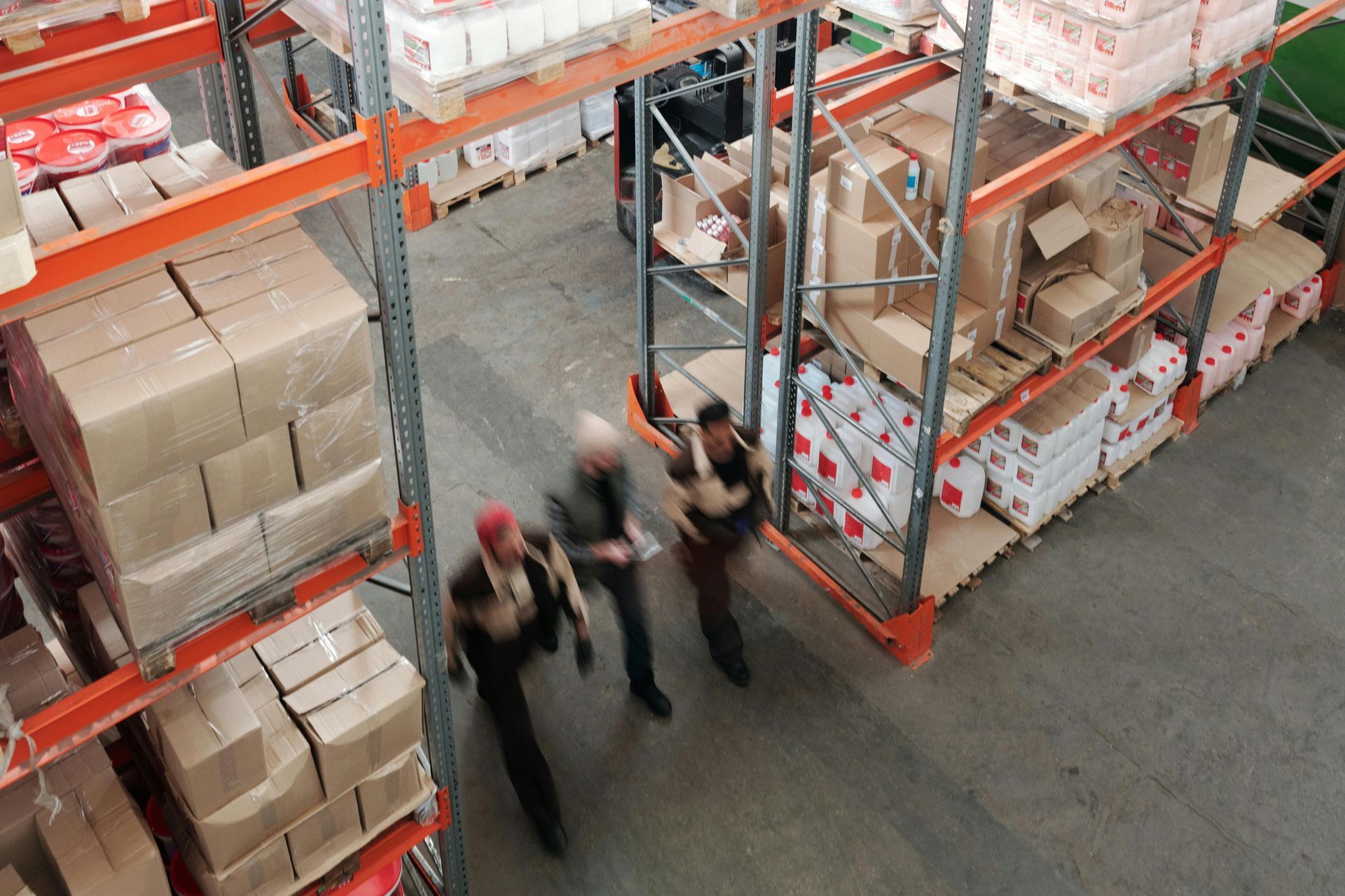 people walking through the rows of warehouse storage shelves.