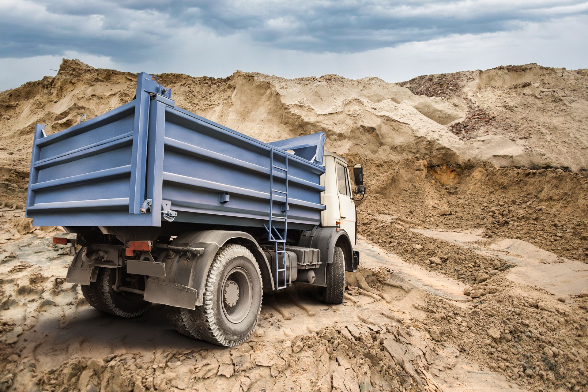 Blue dump truck on a muddy dirt road at a sand excavation site