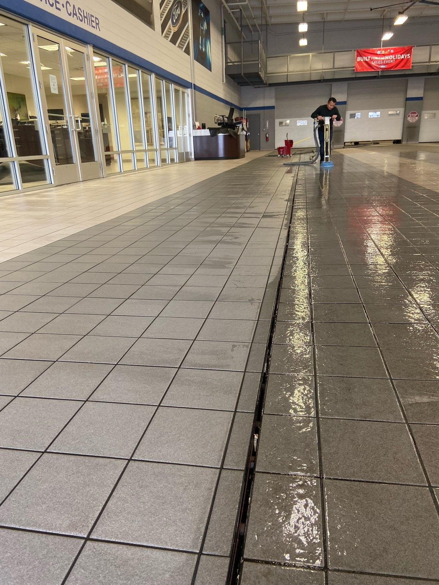 A person uses a floor cleaner on a wet, tiled floor inside a building.