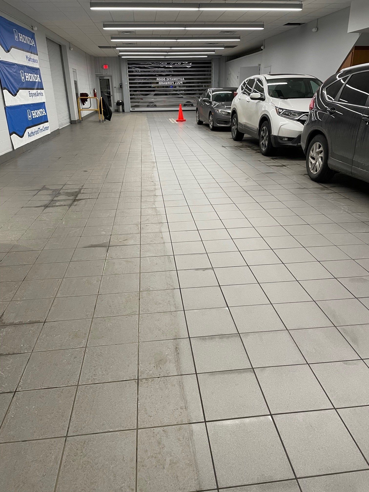 A long hallway with gray tiled floors, cars parked on the right, and a person in the distance.
