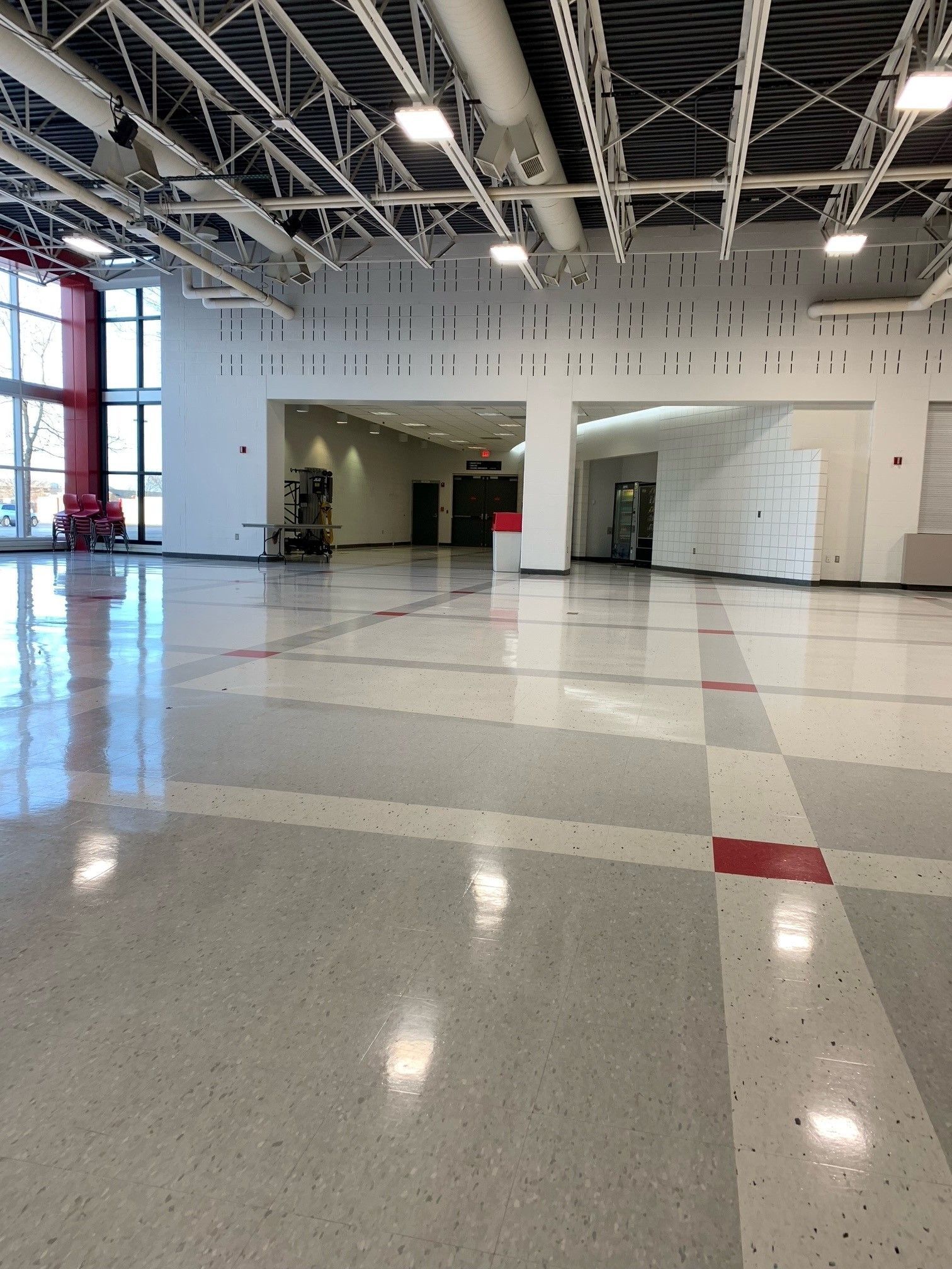 Empty, spacious hall with shiny gray floor. White walls, red accents, and overhead lighting.