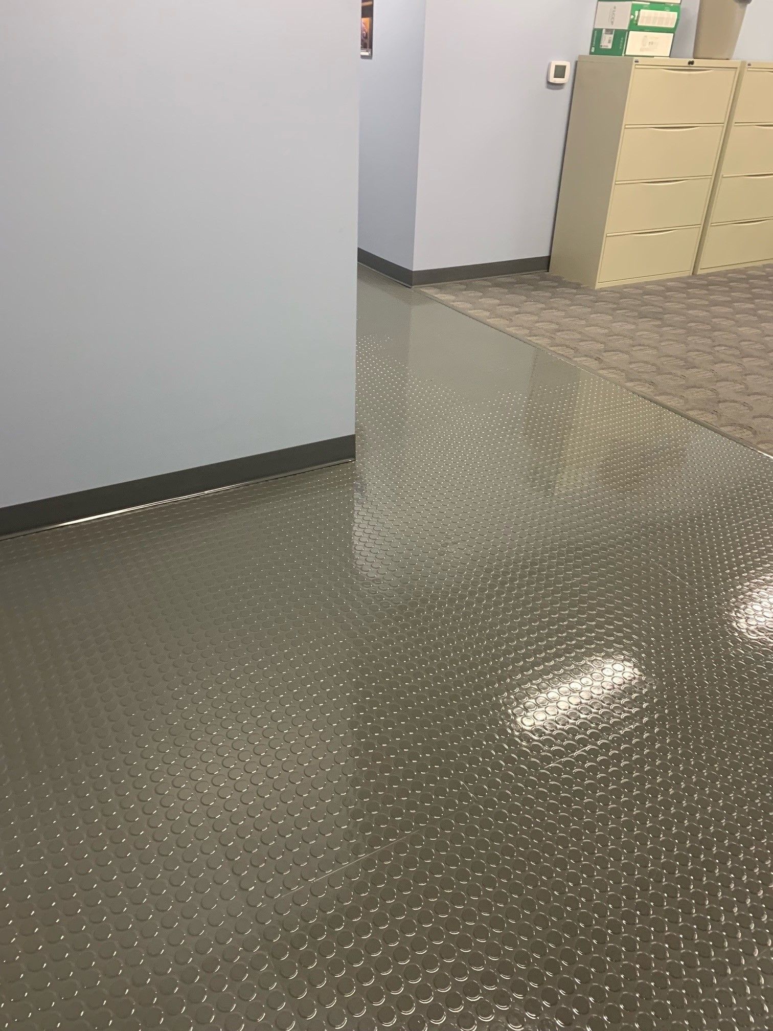 Gray textured floor in a hallway with beige carpet and filing cabinets.