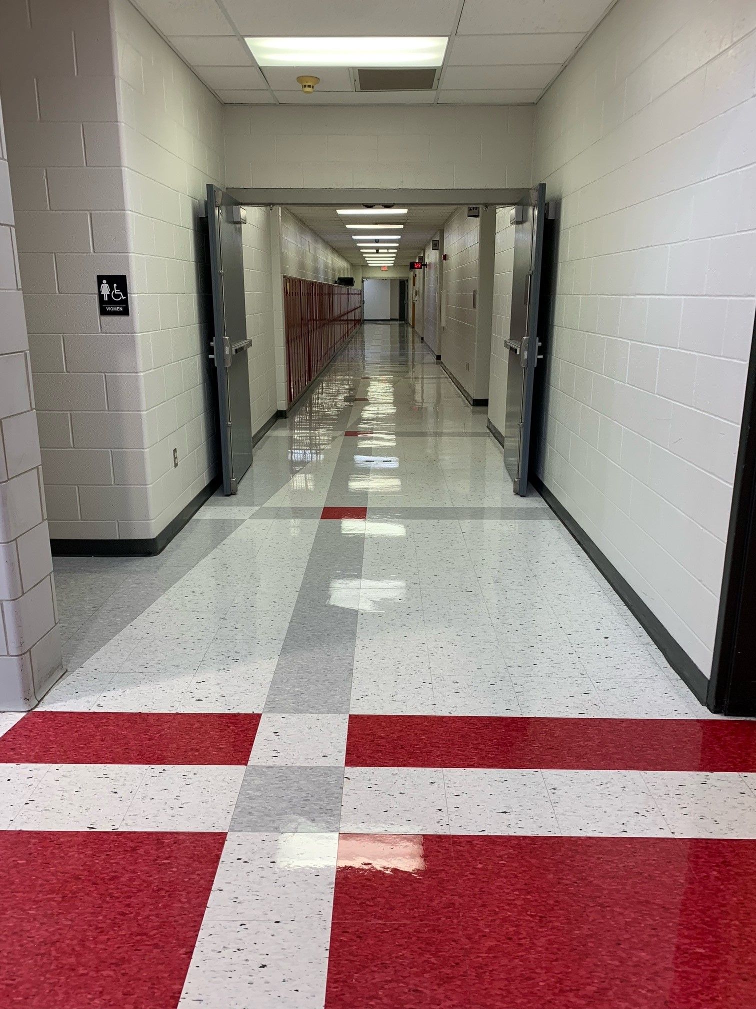 Hallway with red and white tiled floor, lockers, and doors.