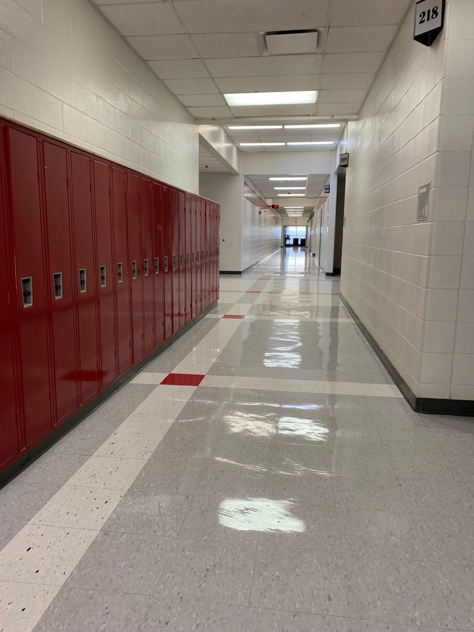 Red lockers line a hallway with a shiny floor and white walls.