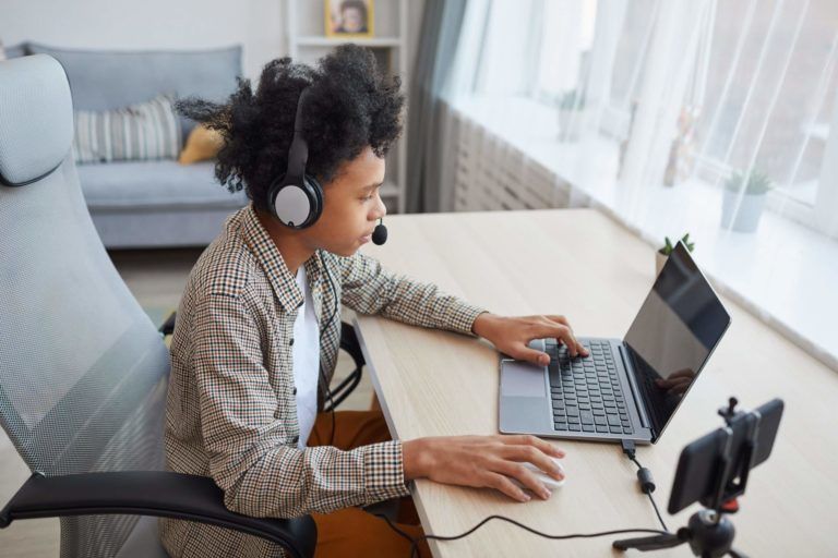 A boy sits at a desk, intently focused on a laptop screen
