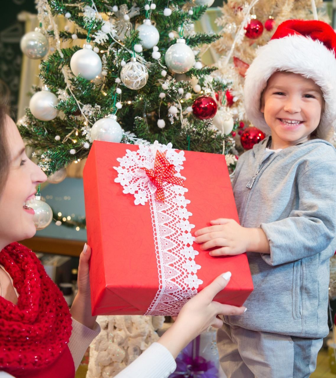 A woman and child are holding a red gift box in front of a christmas tree