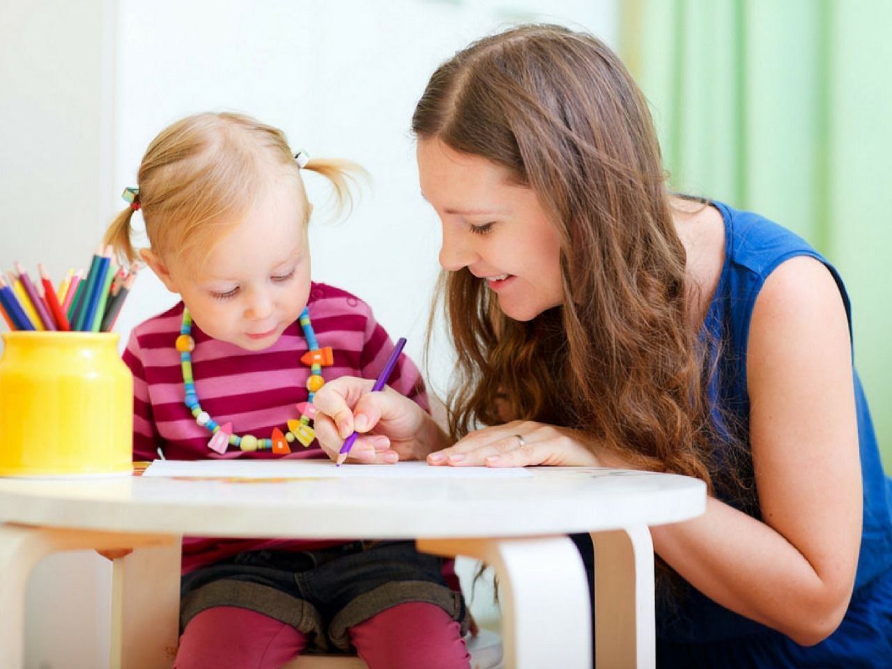 A woman and a little girl are sitting at a table drawing with pencils.