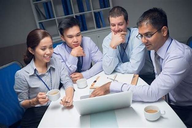 A group of people are sitting around a table looking at a laptop computer.