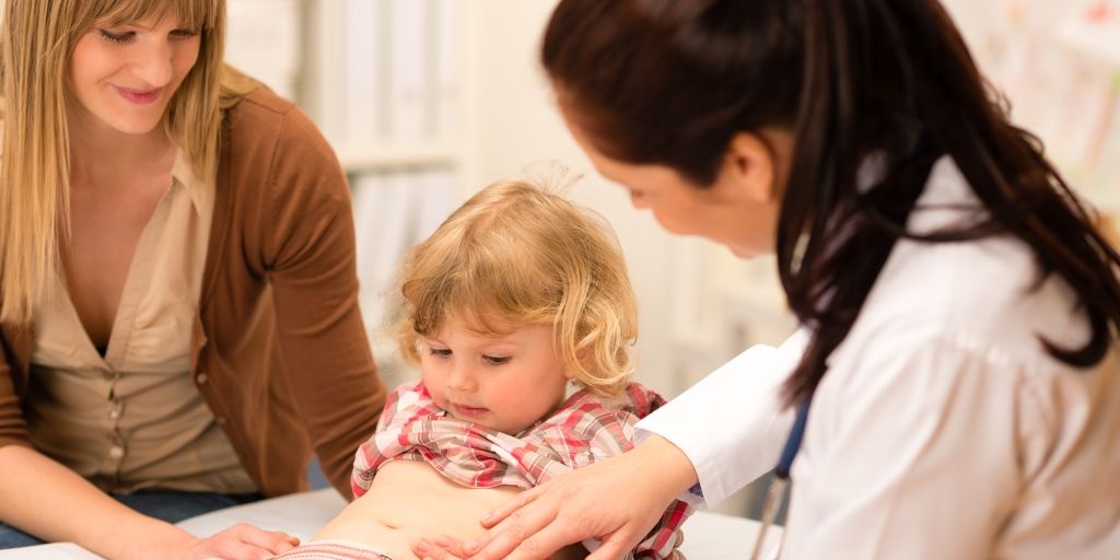 A doctor is examining a little girl 's stomach while a woman looks on.
