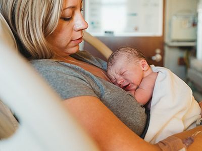 A woman is holding a newborn baby in a hospital bed.