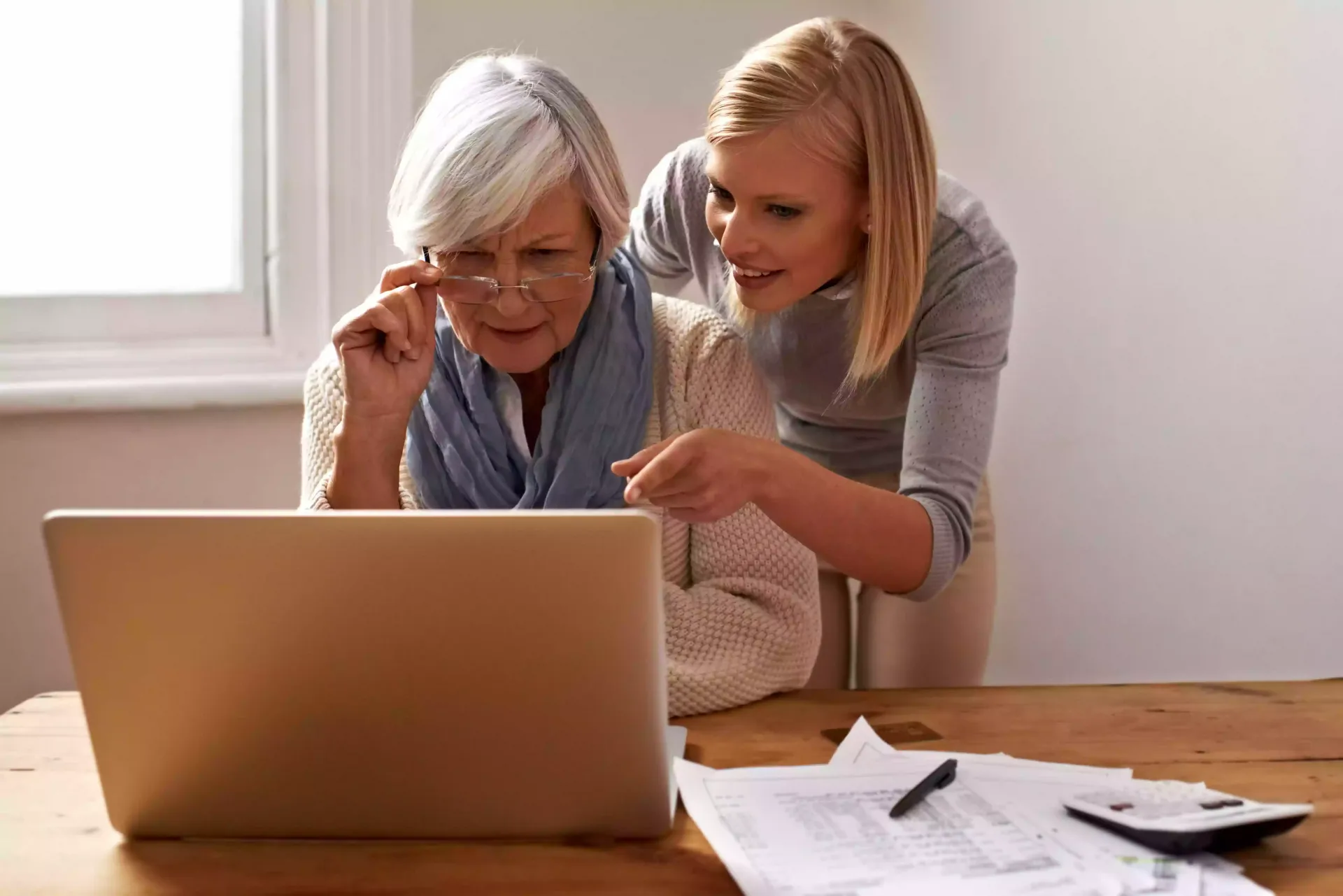 An elderly woman and a young woman are looking at a laptop computer.