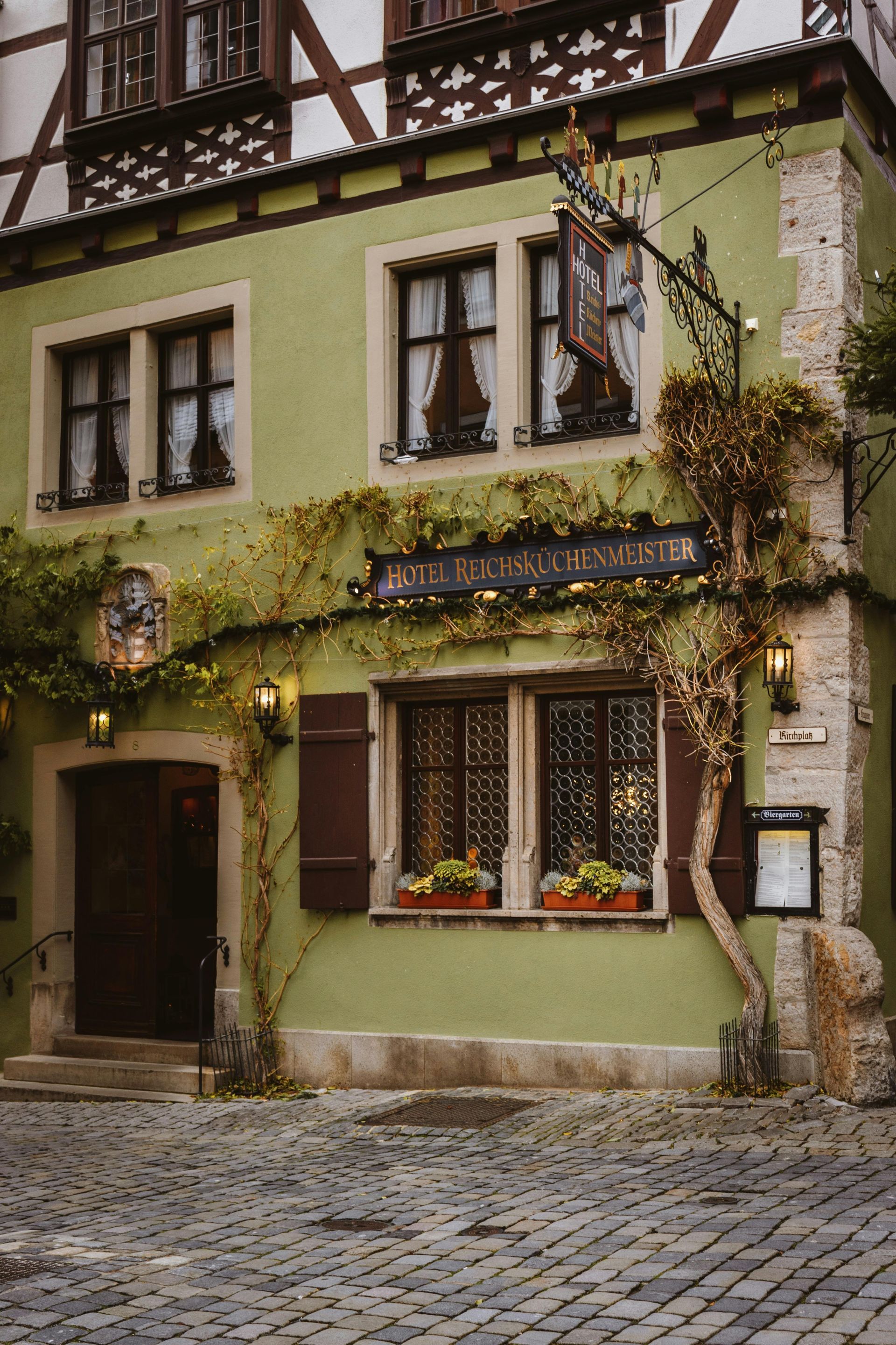 A green building with a sign on the side of it is on a cobblestone street.