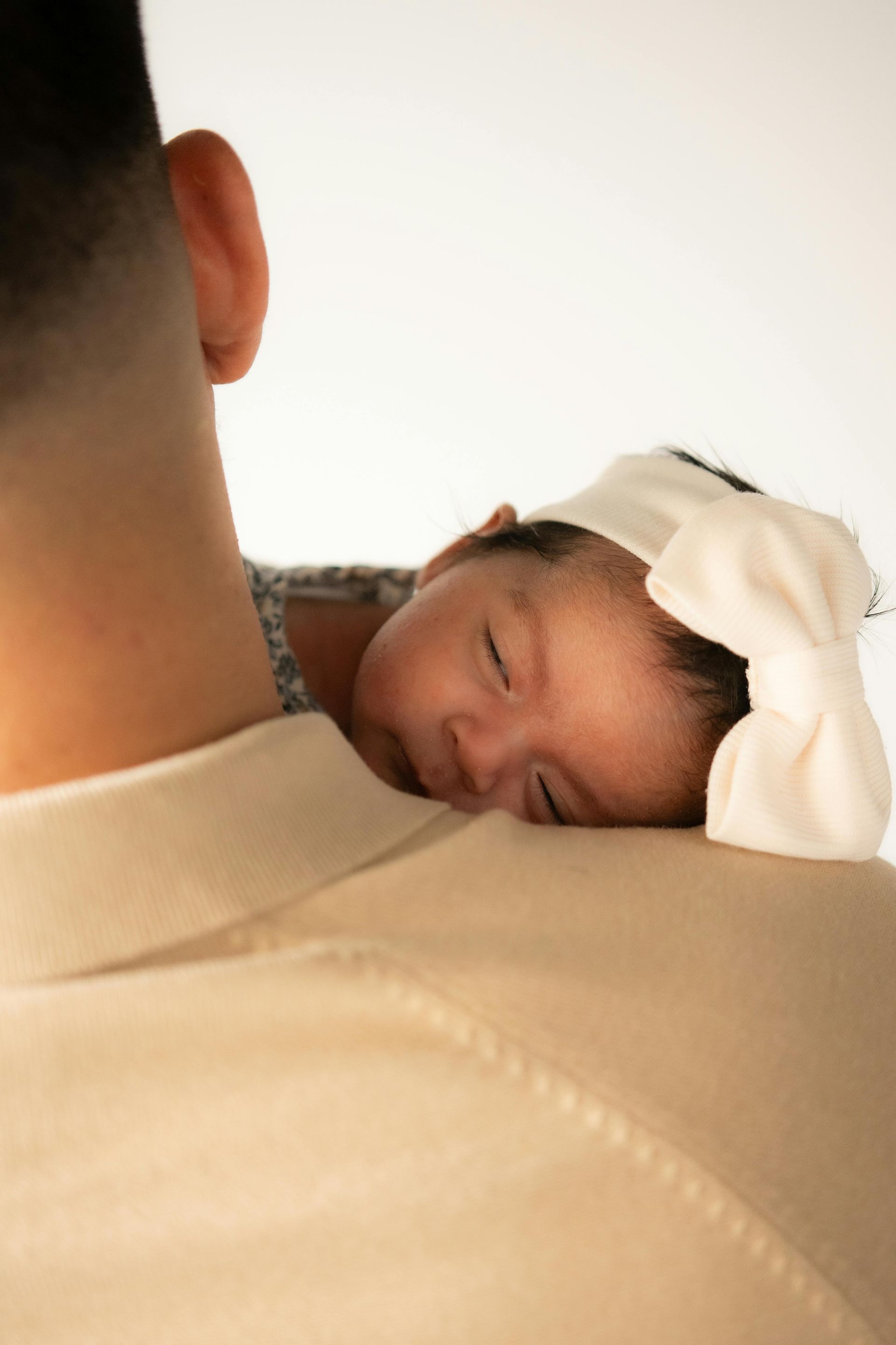 A man is holding a baby girl with a white bow on her head.