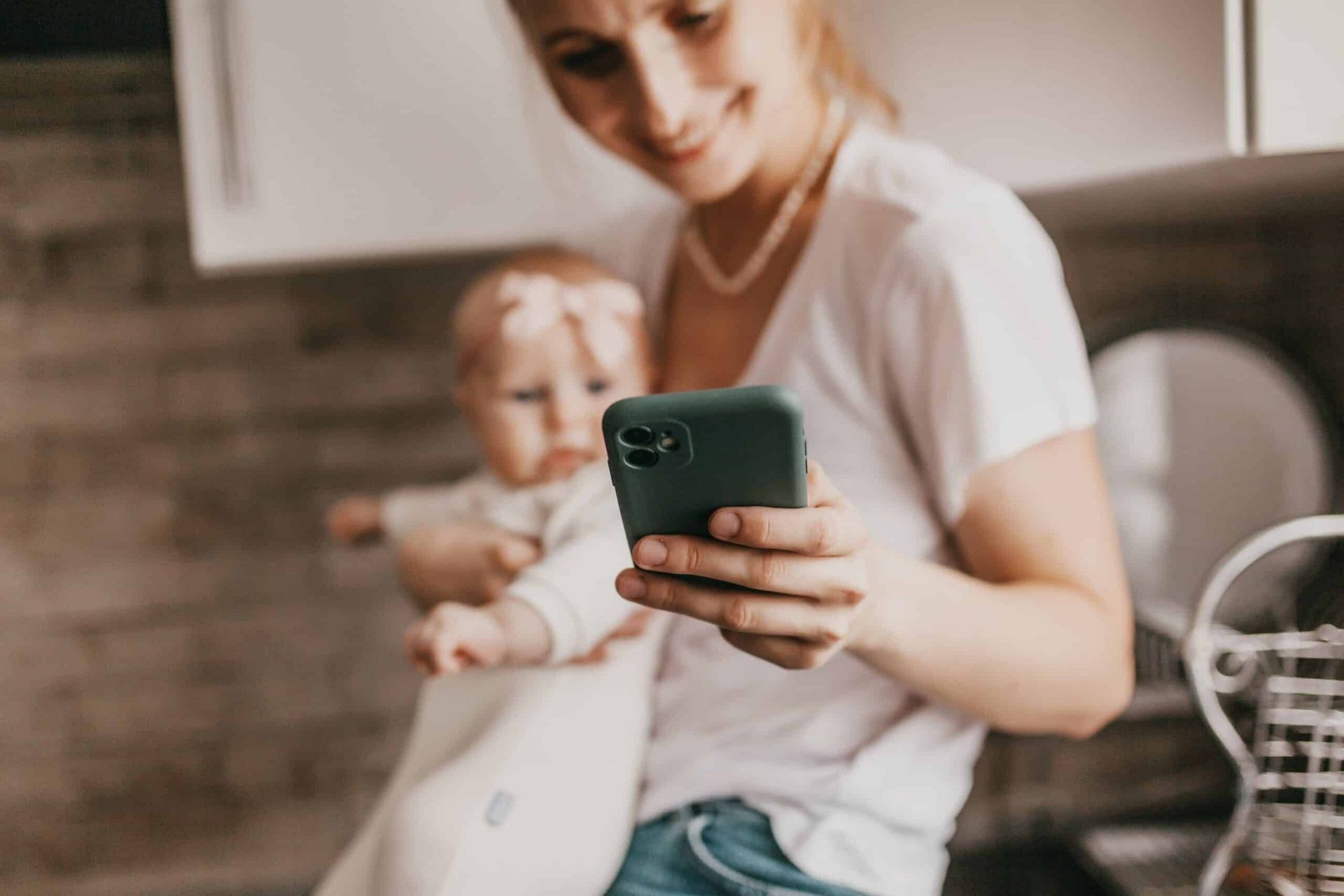 A woman is holding a baby and looking at her phone.