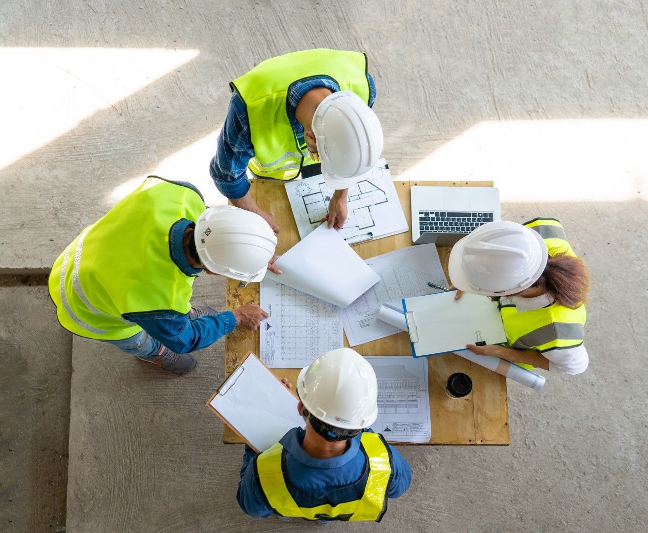 A group of construction workers are sitting around a table looking at a blueprint.