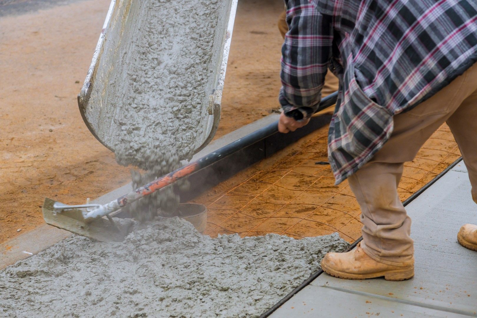 A man is pouring concrete into a sidewalk with a shovel.