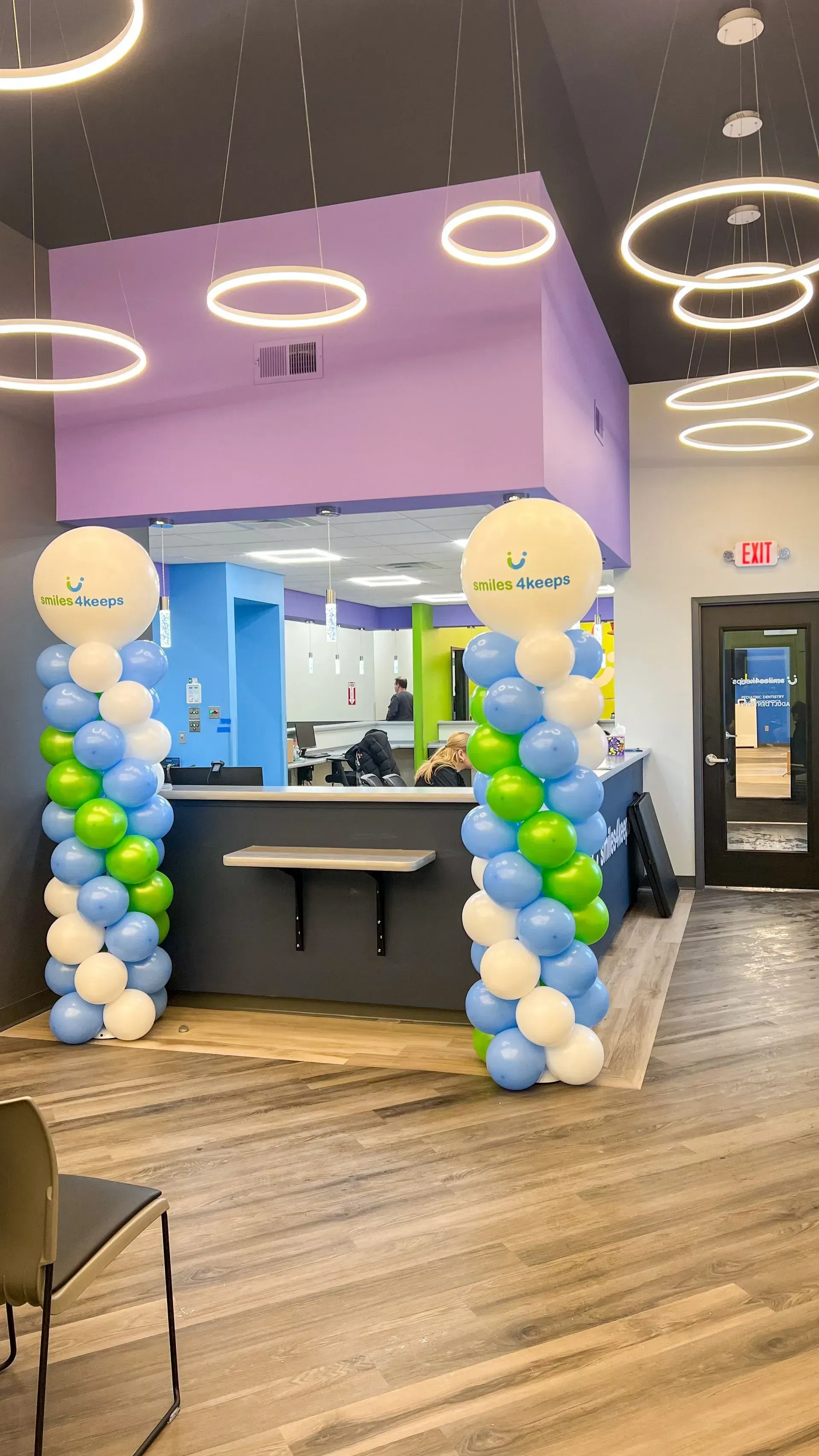 Decorated storefront with blue, white, and yellow balloon columns and ring ceiling lights at an entrance.