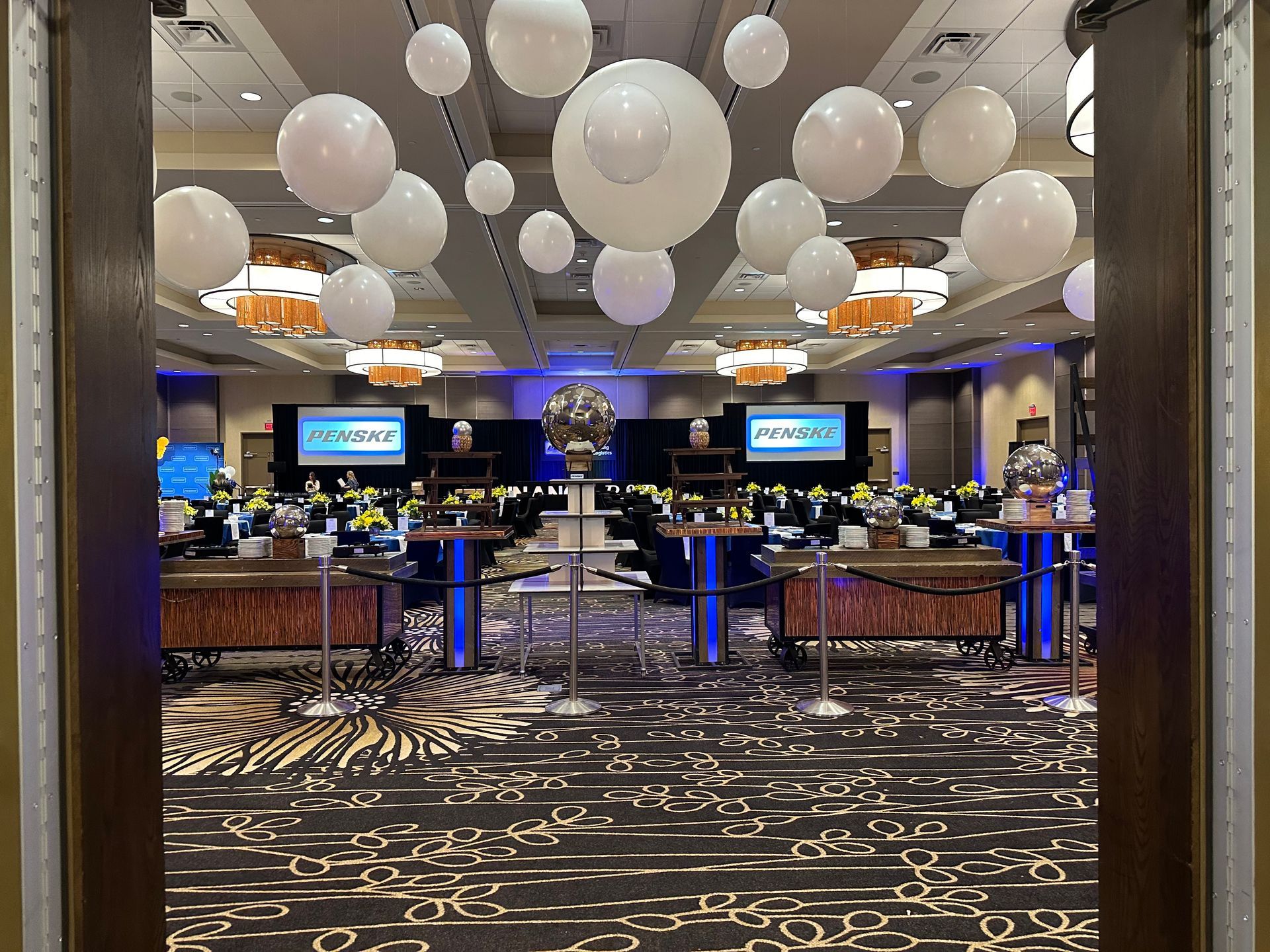Event space decorated with pink balloons, floral arrangements, and round tables with beige linens.