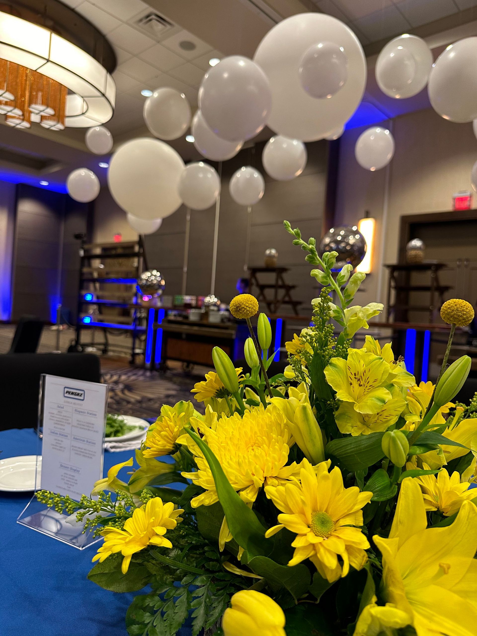 Yellow flowers on a blue table at an elegant event with white balloons and blue lights in the background