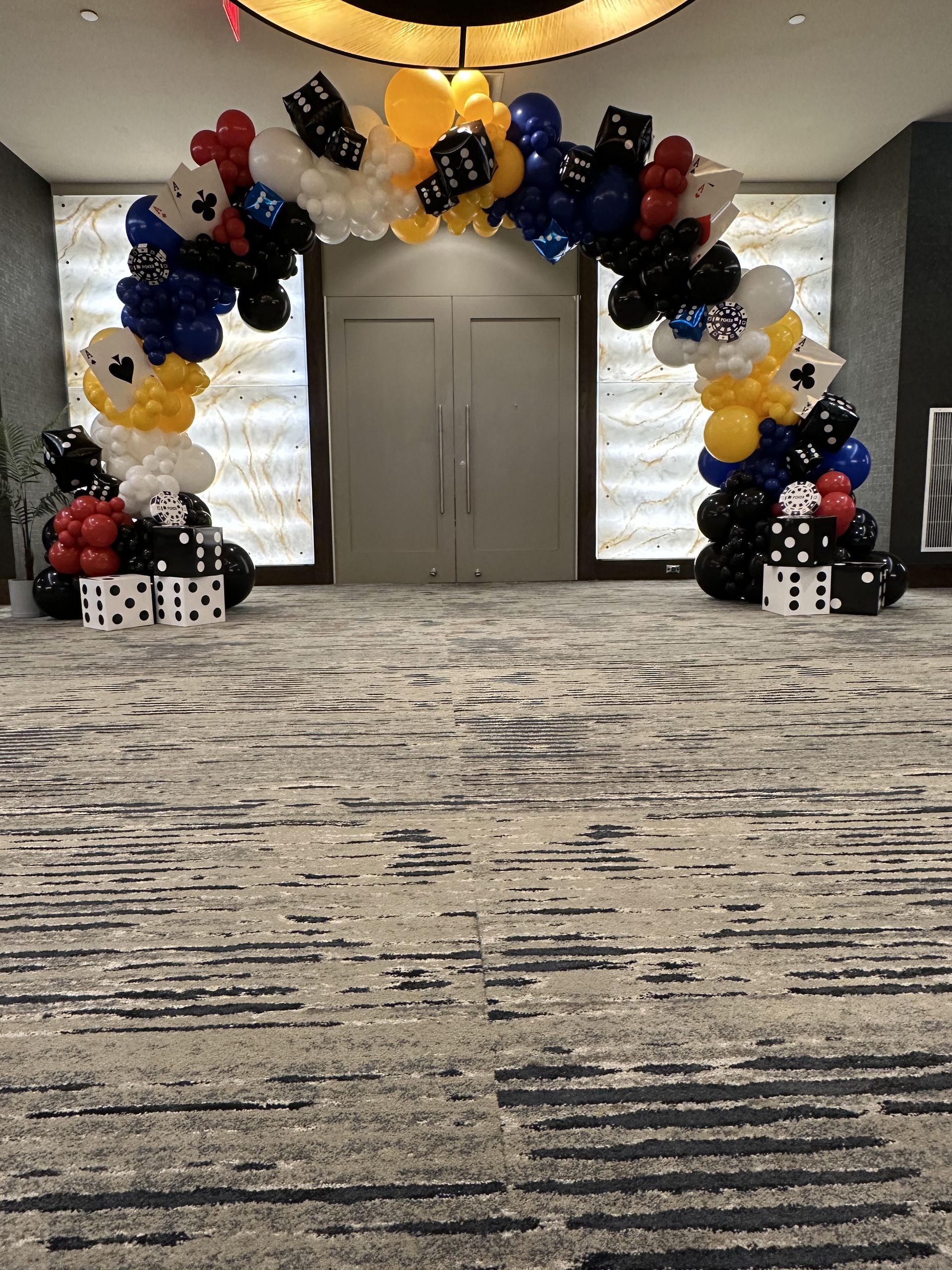 Balloon arch entrance with black, yellow, white, and blue Mickey Mouse balloons, domino accents, and gray carpet.