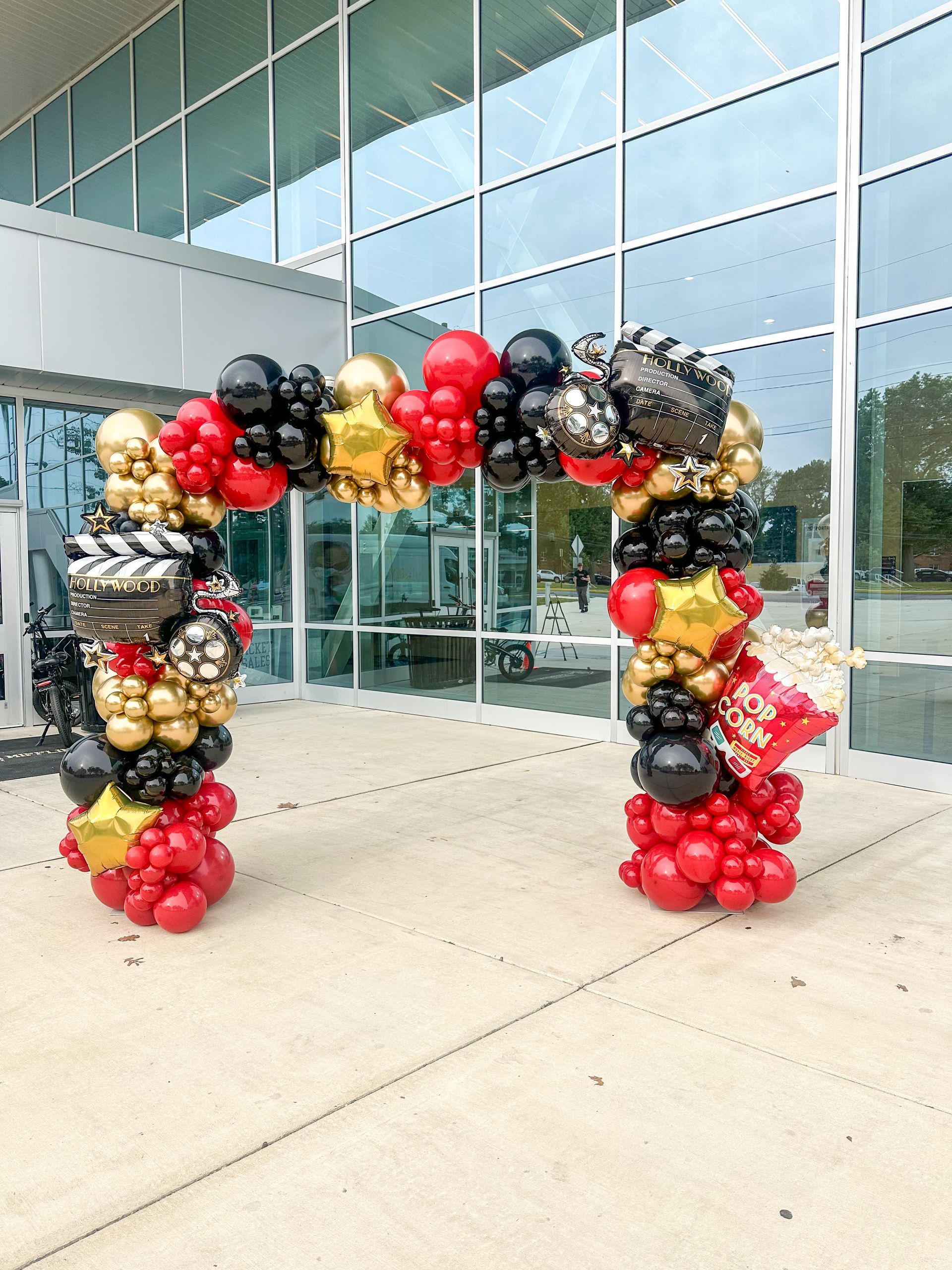 Balloon arch in red, black, gold, and silver, shaped like a doorway, likely for an event.
