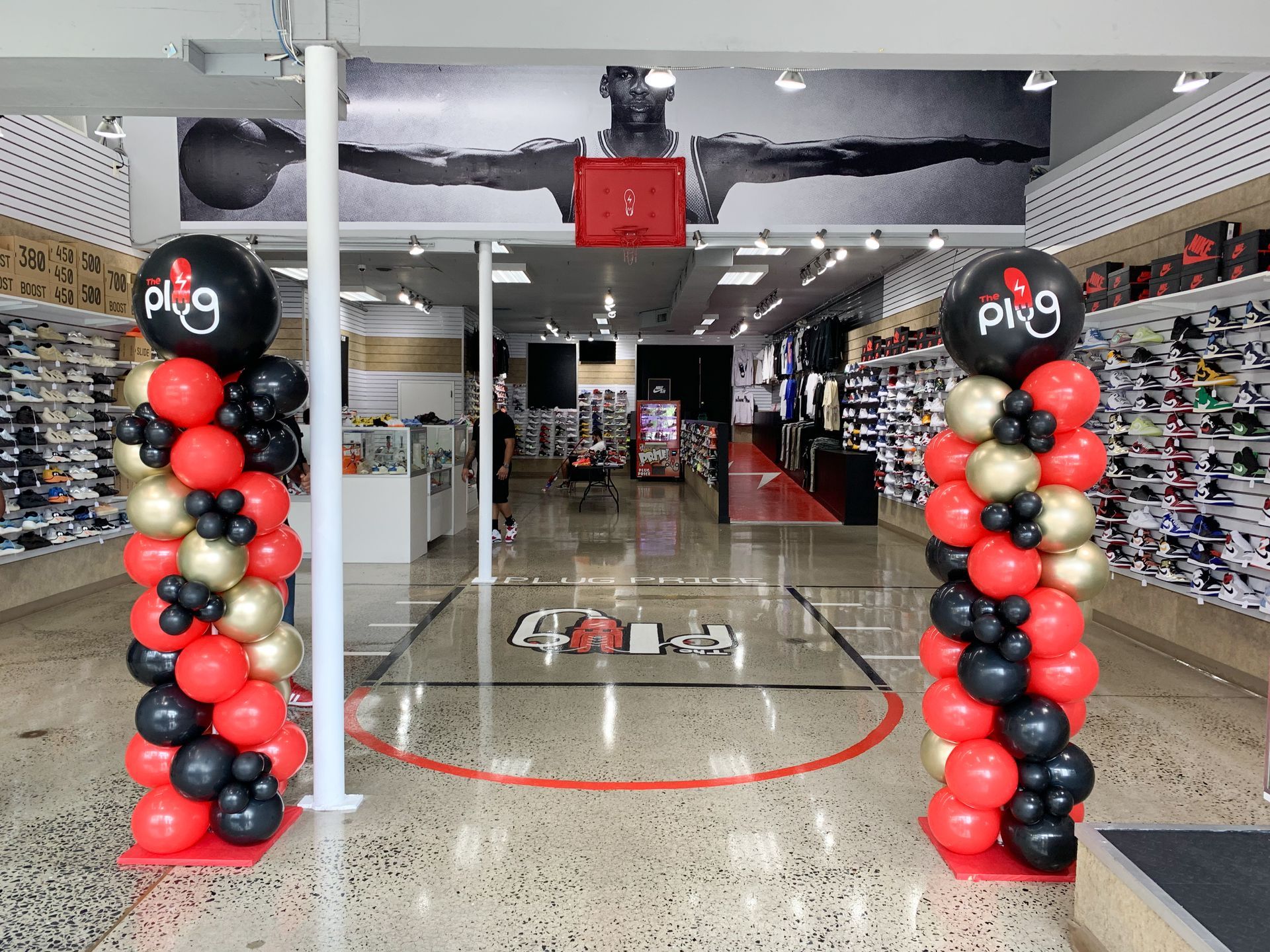 Shoe store entrance with red, black, and gold balloon columns. A basketball court design is on the floor.
