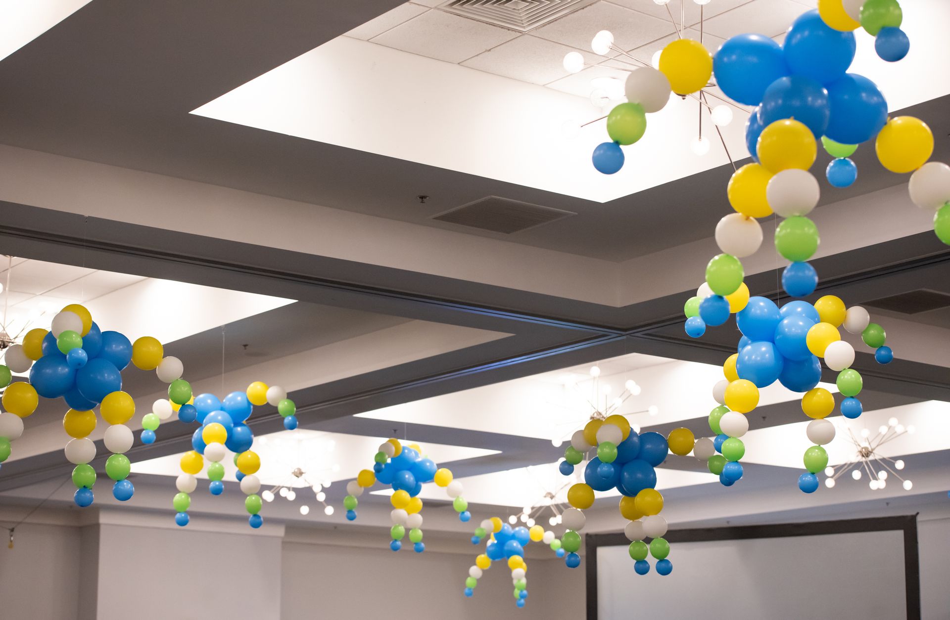 Decorated ceiling with blue, yellow, green, and white balloon arrangements in a room.
