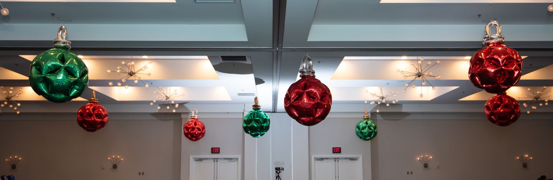 Christmas ornaments hanging from the ceiling in a room. Red and green ornaments are strung across the space.