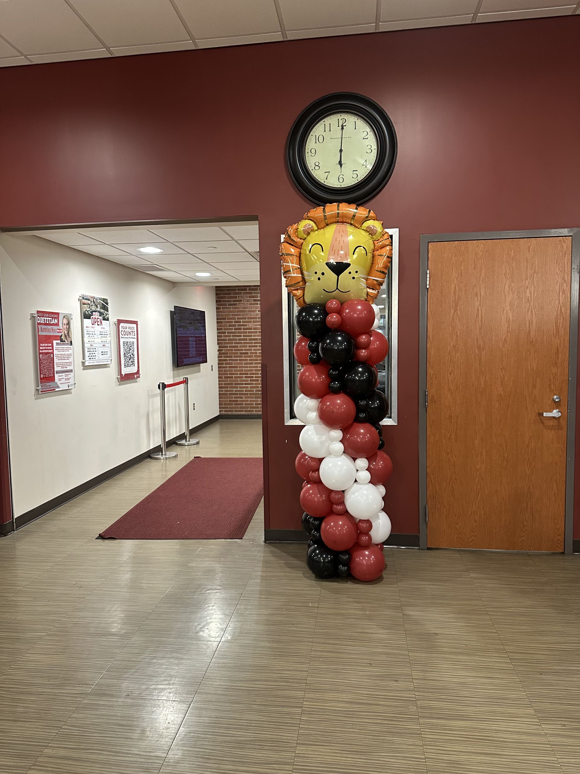Hallway with a balloon column topped with a lion's face. Clock on wall above.