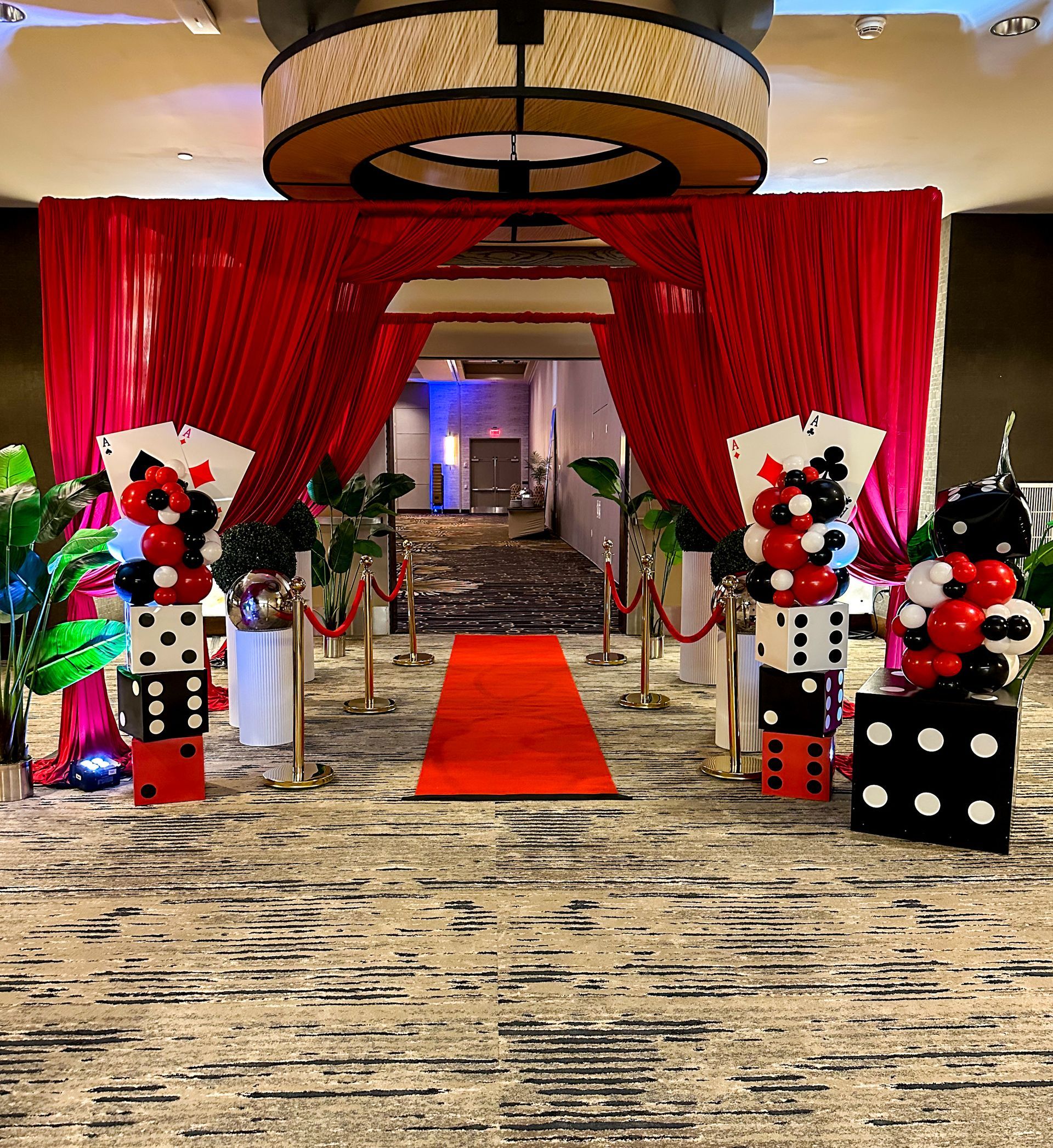 Casino-themed event entrance with red carpet, curtains, dice, and playing card balloon sculptures.