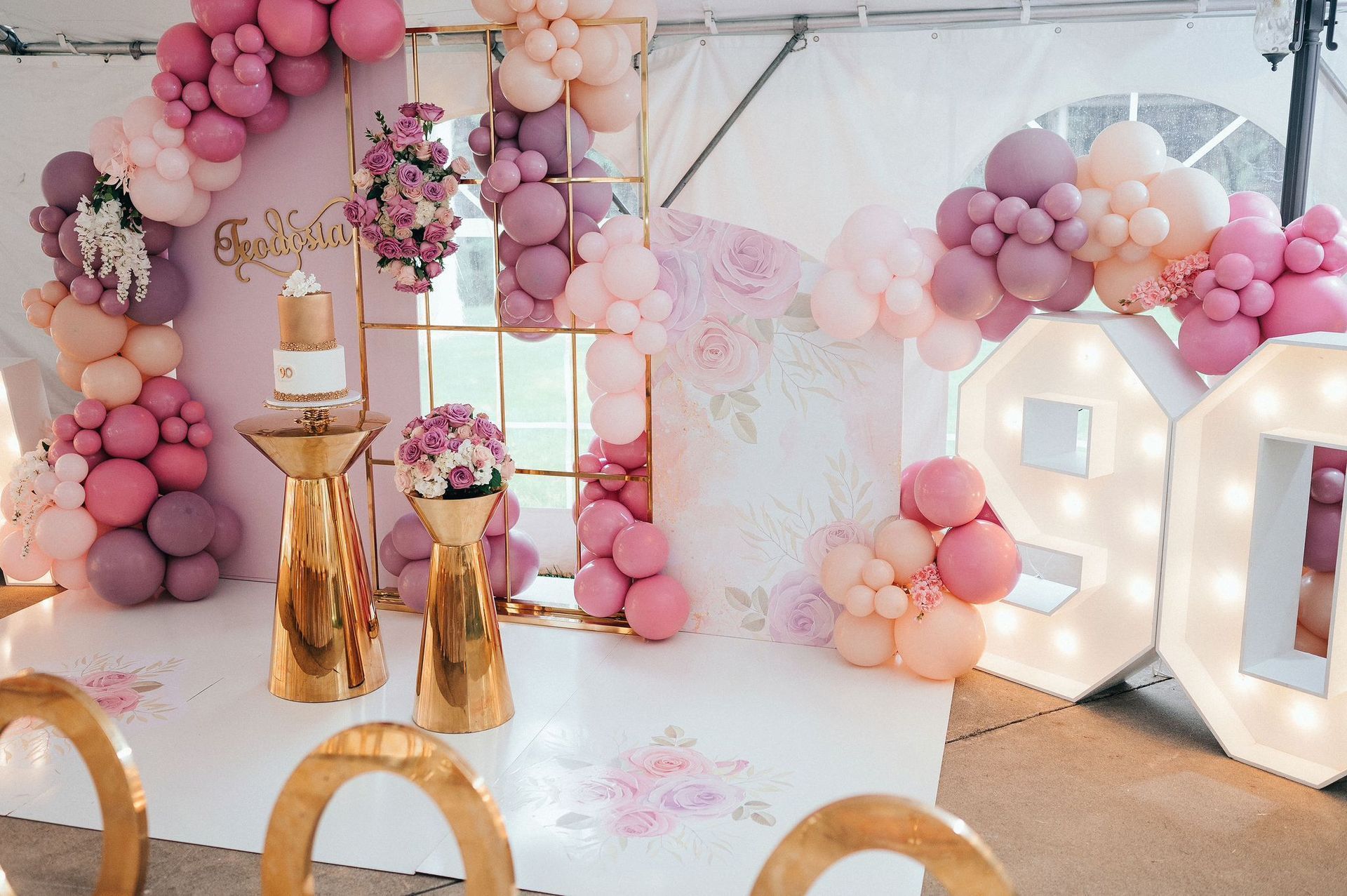 Party decor with balloon arch, cake, flowers, and lit-up