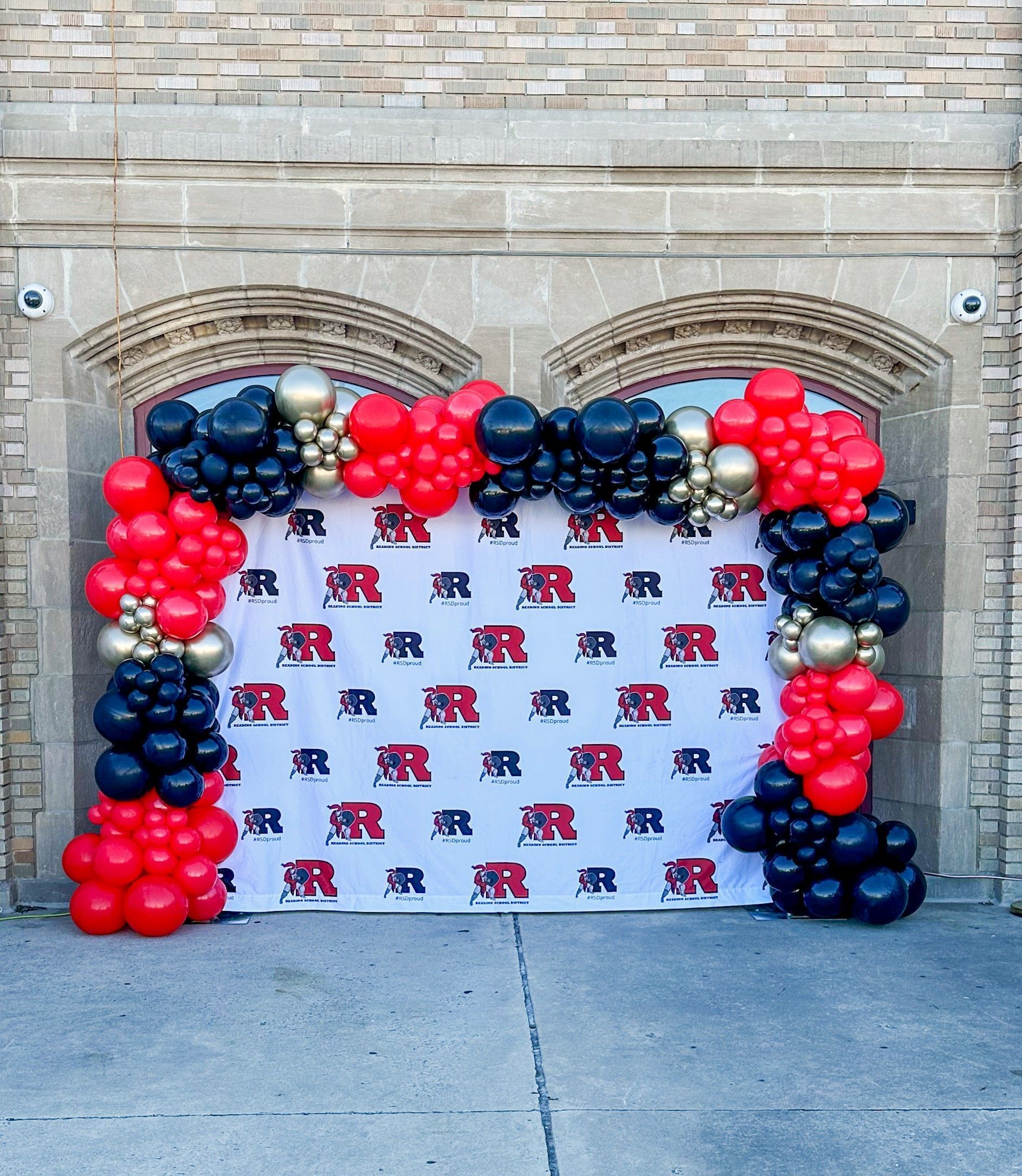 Photo booth backdrop with red, black, and gold balloon arch; logo backdrop with the letters