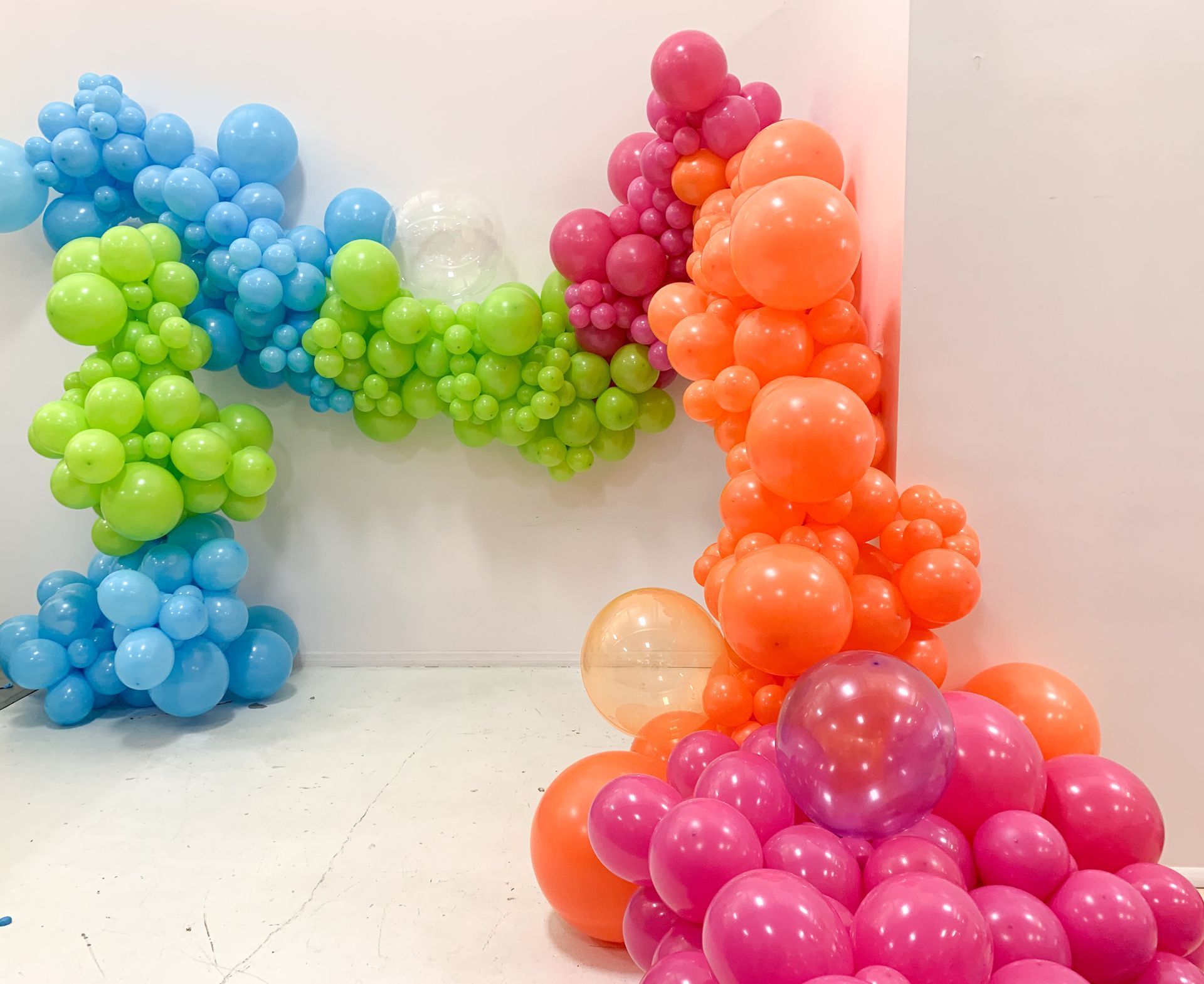 Colorful balloon arch cascading down a white wall, featuring shades of blue, green, orange, pink and white.