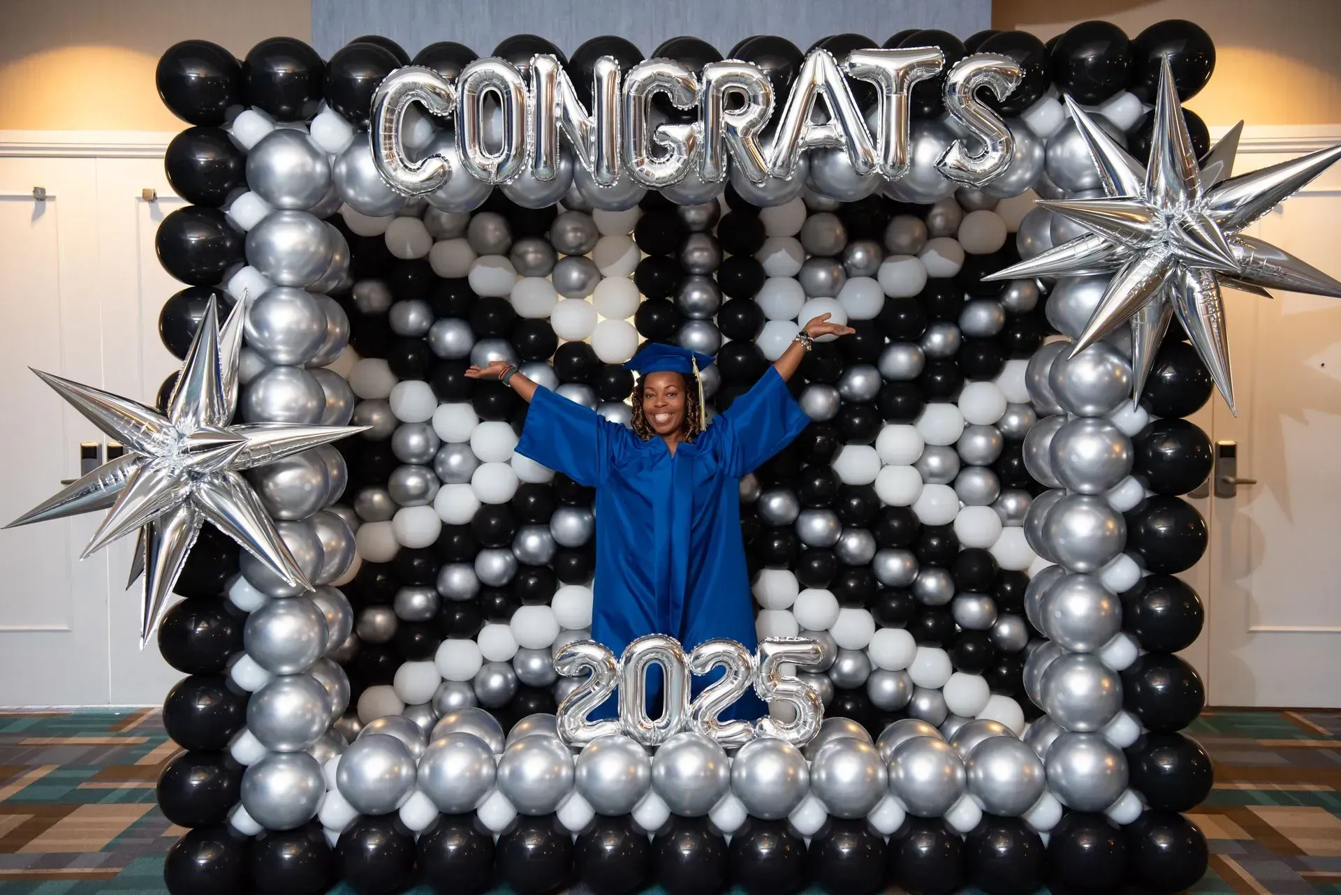 Person in blue graduation gown inside a balloon frame that reads