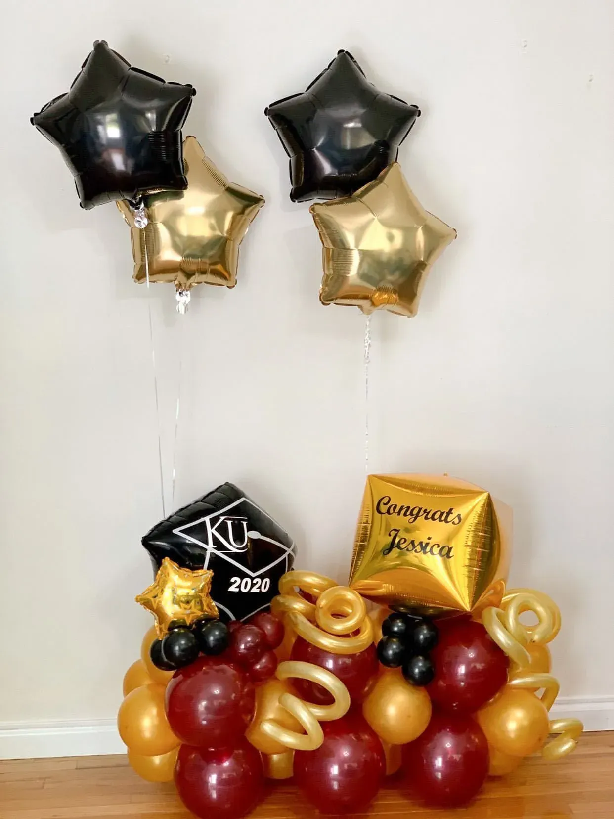 Graduation balloon arrangement: Black, gold, and maroon balloons with star and cap-shaped balloons.