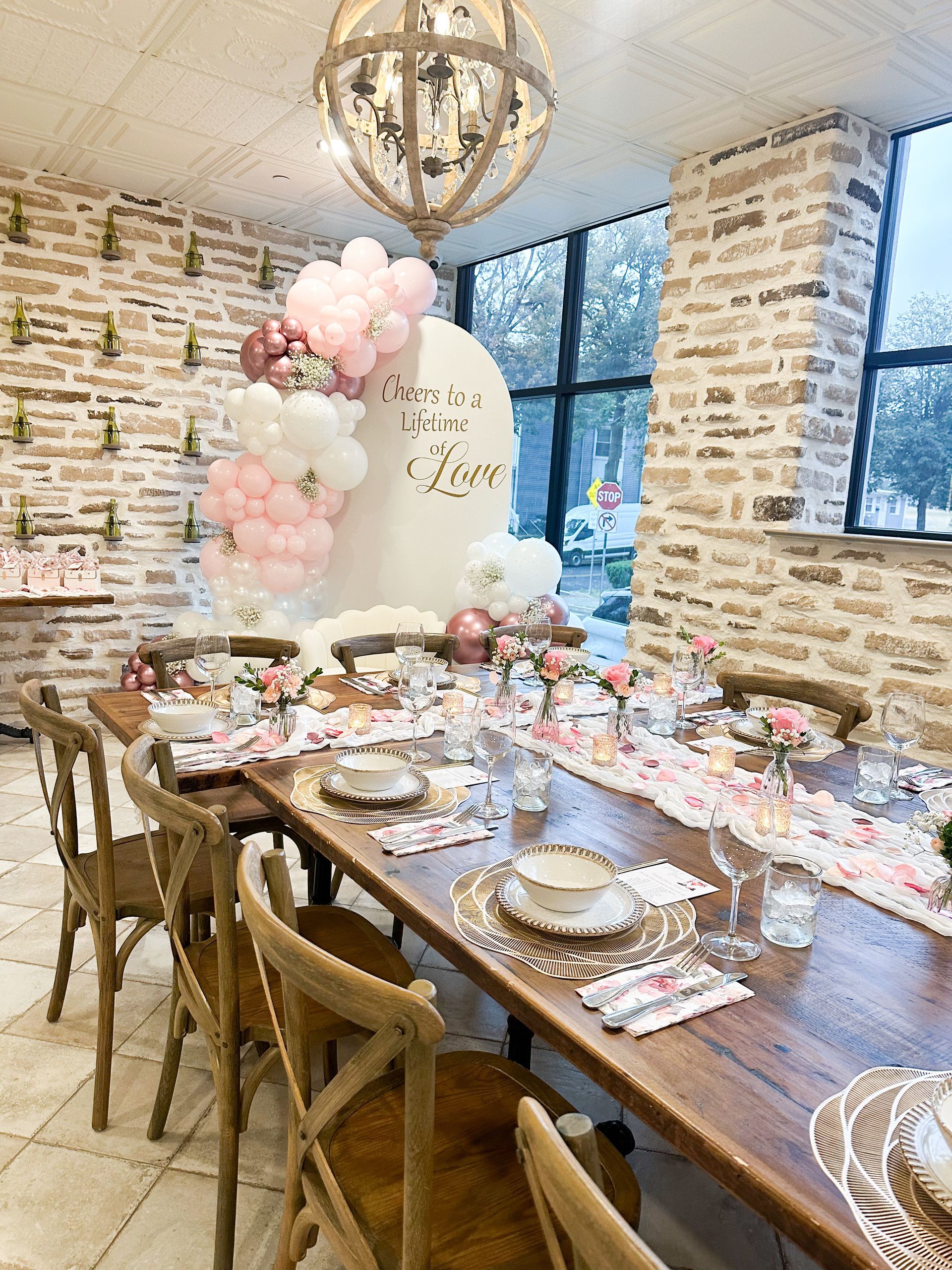 Dining table set for a party, with balloons and floral decorations in a room with stone walls.